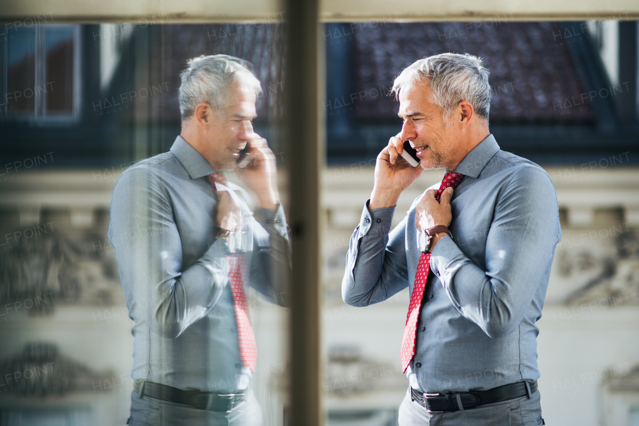 A mature businessman with smartphone standing on a terrace in an office in city, making a phone call.