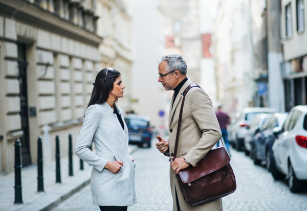 Mature man and young woman business partners standing outdoors in city of Prague, talking.