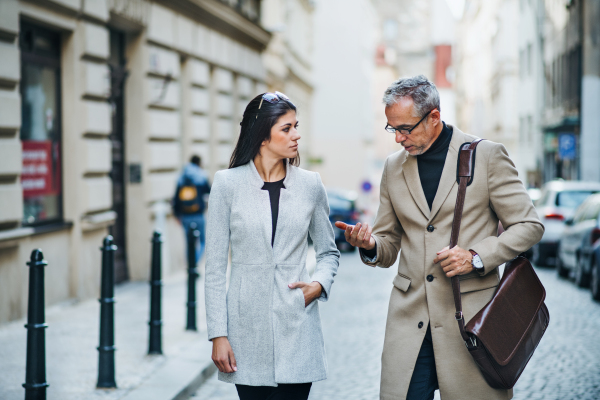 Mature man and young woman business partners walking outdoors in city of Prague, talking.