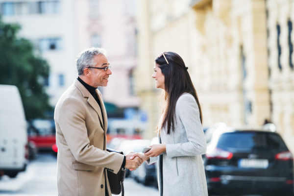 Mature man and young woman business partners standing outdoors in city of Prague, shaking hands.