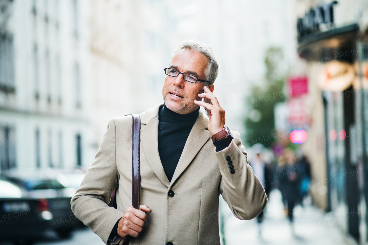 A mature businessman standing on a street in city, using smartphone.