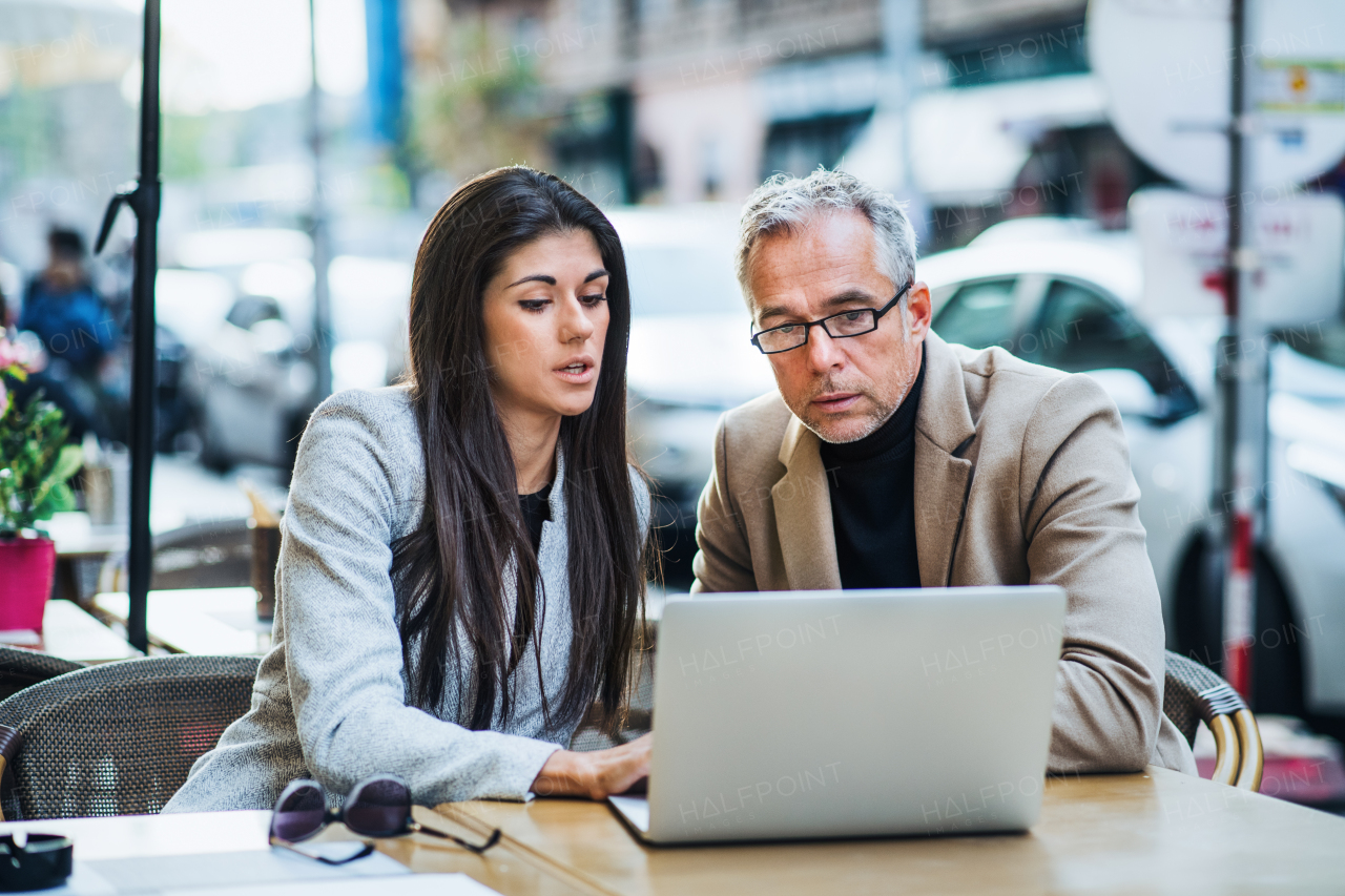 Man and woman business partners with laptop sitting in a cafe in city, discussing issues.