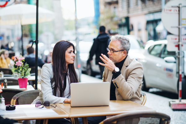 Man and woman business partners with laptop sitting in a cafe in city, discussing issues.