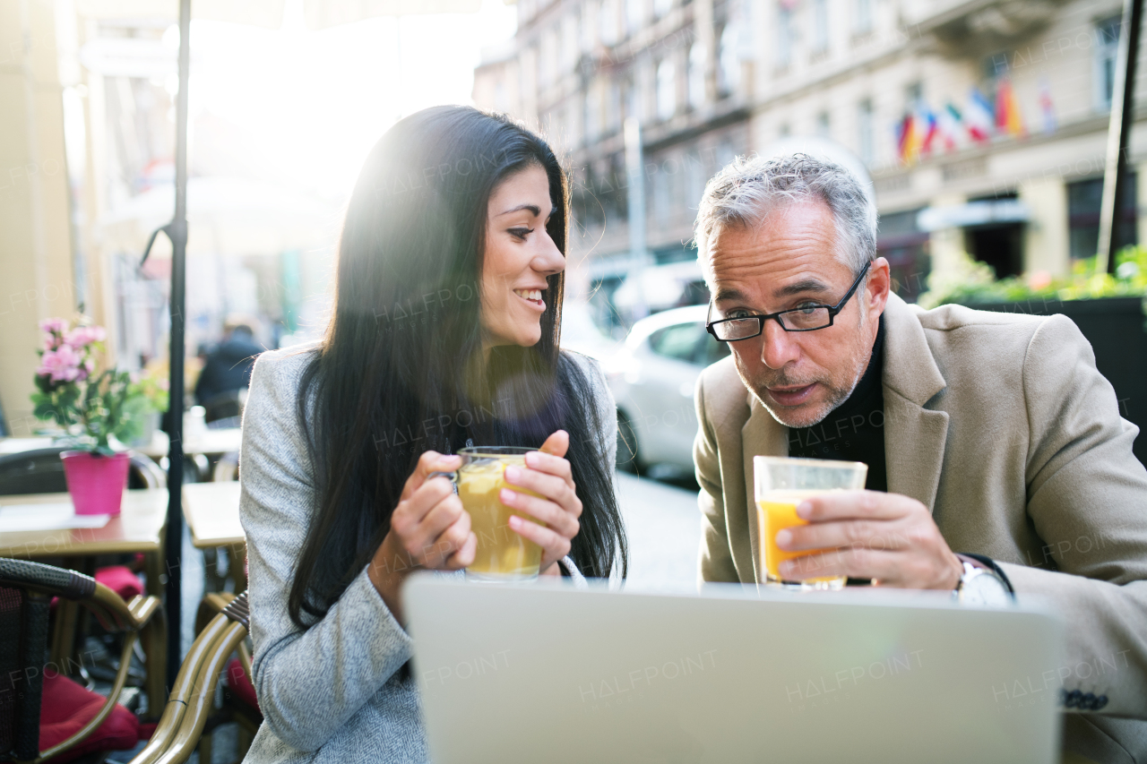 Man and woman business partners with laptop and drinks sitting in a cafe in city, talking.