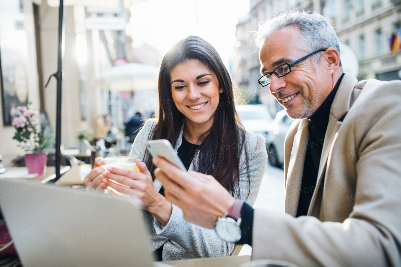 Man and woman business partners with laptop and smartphone sitting in a cafe in city, talking.