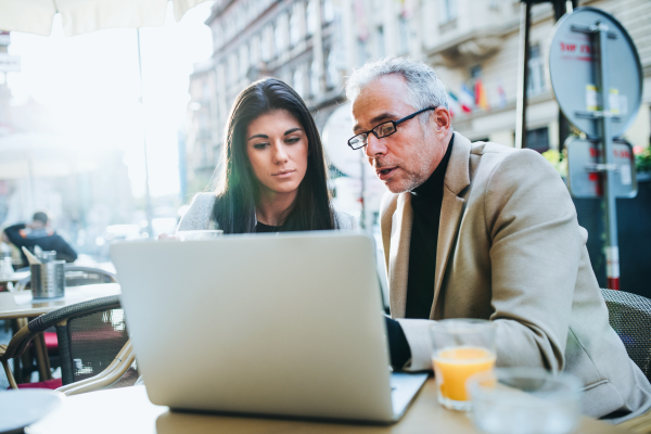 Man and woman business partners with laptop and drinks sitting in a cafe in city, talking.