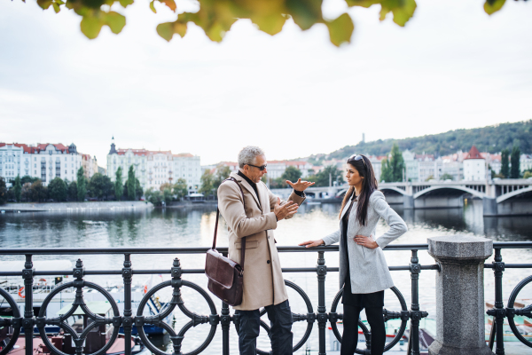 Mature man and young woman business partners standing by a river in city of Prague, talking.