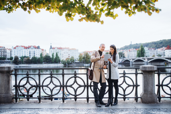 Man and woman business partners with tablet standing by a river in city of Prague, talking. Copy space.