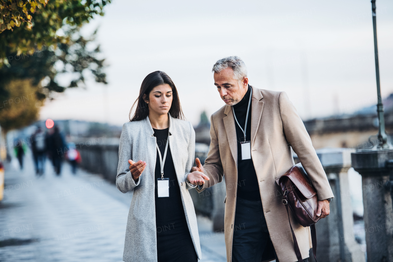 Mature man and young woman business partners walking by a river in city of Prague, talking.