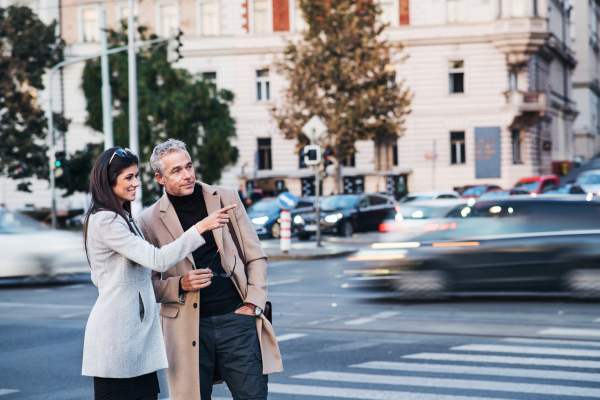 Cheerful man and woman business partners crossing road outdoors in city of Prague, talking. Copy space.