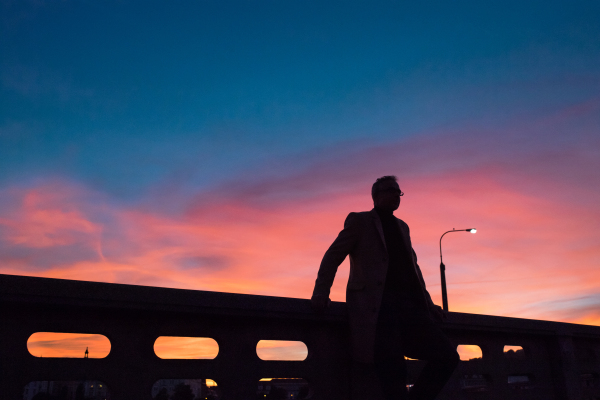 A silhouette of businessman standing on a bridge at dusk. Copy space.