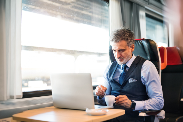 Handsome mature businessman travelling by train. A man with laptop and a coffee.