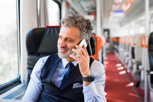 Handsome mature businessman travelling by train. A man with smartphone, making a phone call.