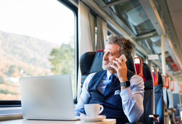 Handsome mature businessman travelling by train. A man with smartphone, making a phone call.