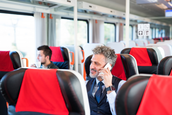 Handsome mature businessman travelling by train. A man with smartphone, making a phone call.