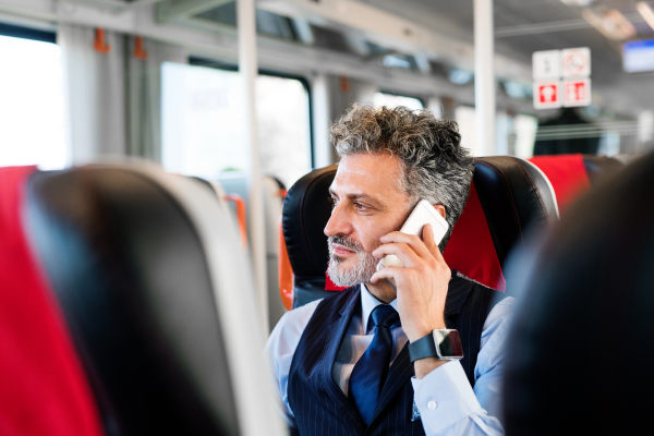 Handsome mature businessman travelling by train. A man with smartphone, making a phone call.