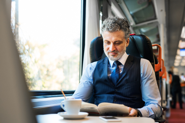 Handsome mature businessman travelling by train, reading a book.