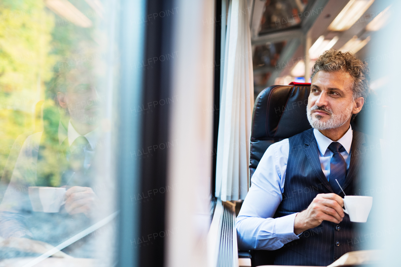 Handsome mature businessman travelling by train. A man looking out of the window, holding a coffee.