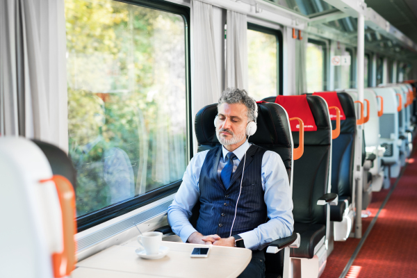 Handsome mature businessman travelling by train. A man with smartphone and headphones, listening to music.