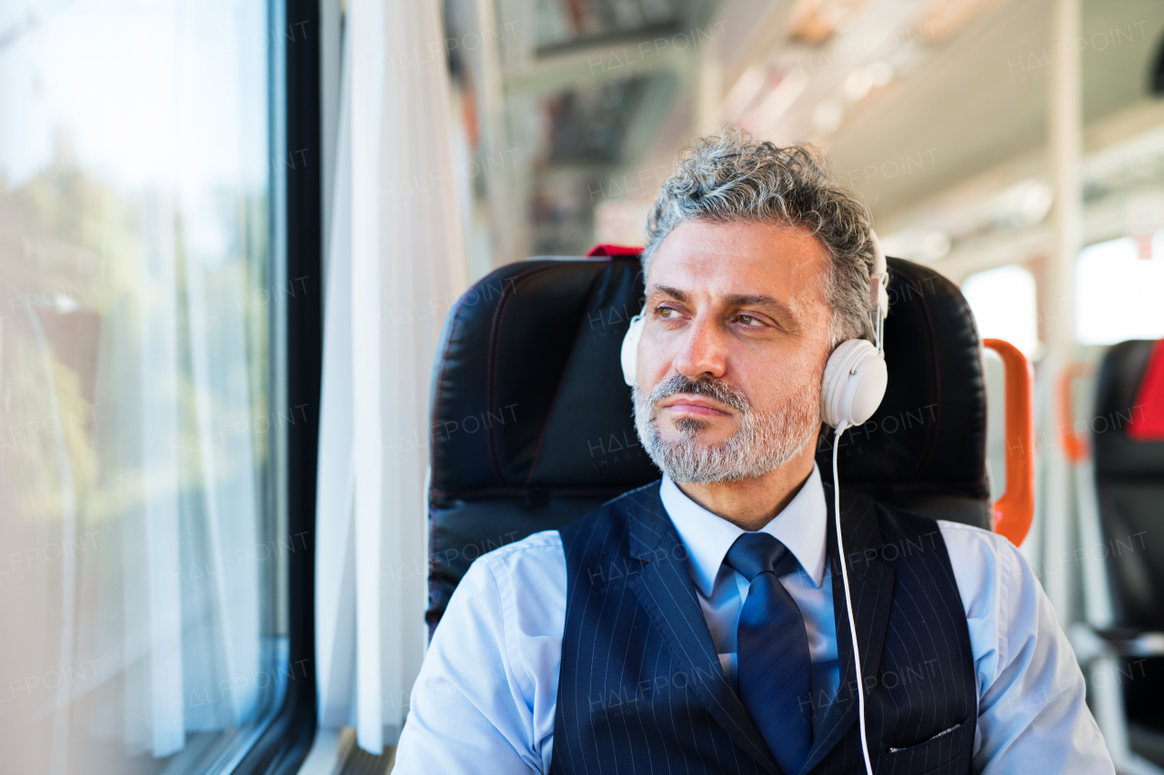 Handsome mature businessman travelling by train. A man with headphones, listening to music.