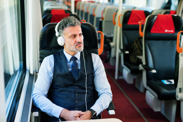 Handsome mature businessman travelling by train. A man with headphones, listening to music.