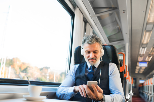 Handsome mature businessman travelling by train. A man with smartphone and headphones, listening to music.