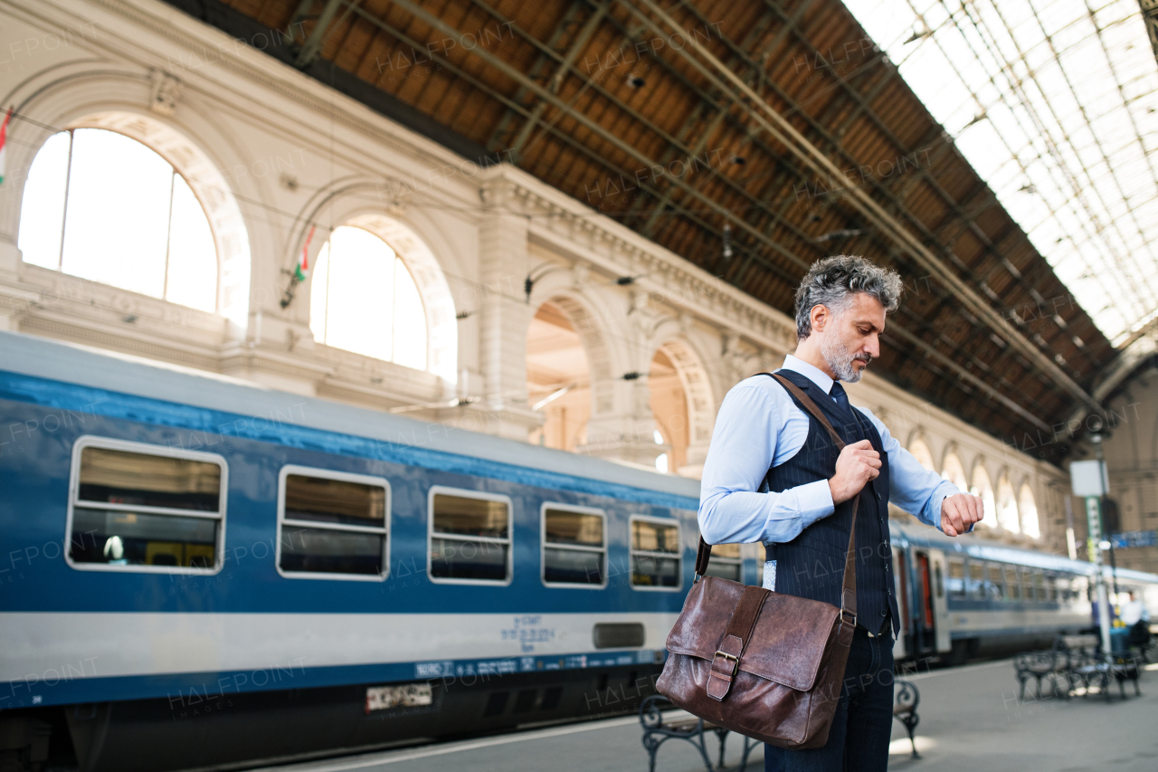 Handsome mature businessman in a city. Man waiting for the train at the railway station, checking times.