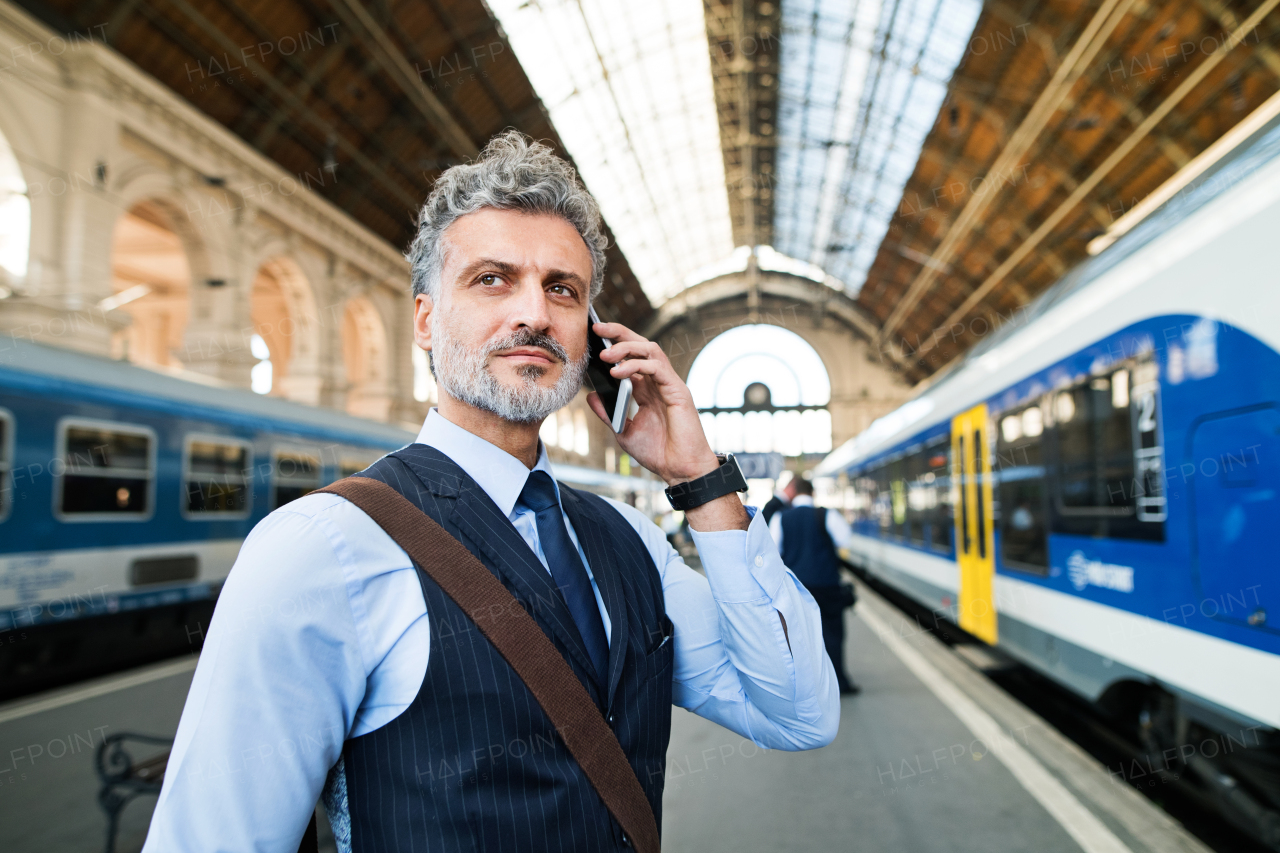 Handsome mature businessman with smartphone in a city. Man waiting for the train at the railway station, making a phone call.