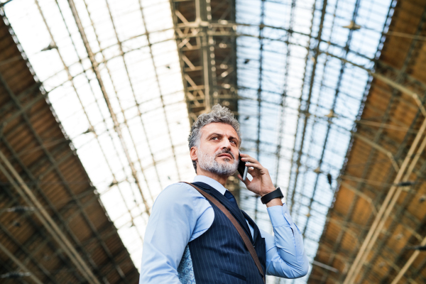 Handsome mature businessman with smartphone in a city. Man waiting for the train at the railway station, making a phone call.