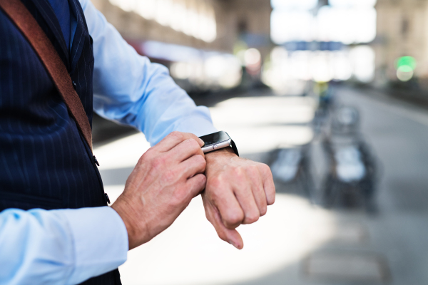 Unrecognizable businessman in a city. Man waiting for the train at the railway station, checking times.