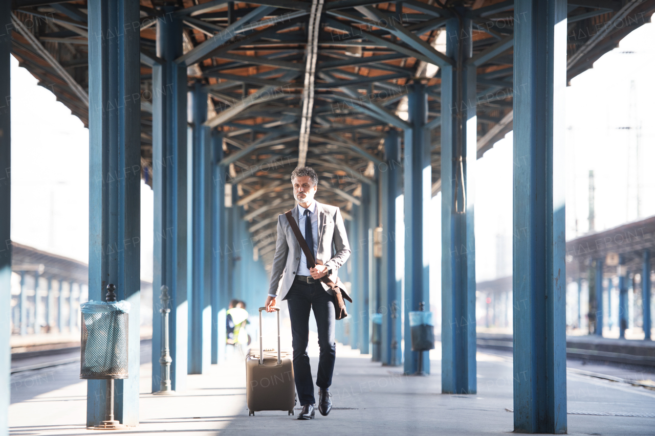 Handsome mature businessman in a city. Man walking on the railway platform on the train station.