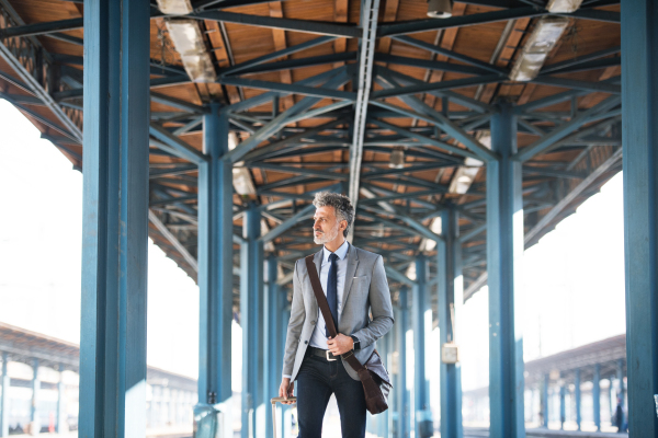 Handsome mature businessman in a city. Man walking on the railway platform on the train station.