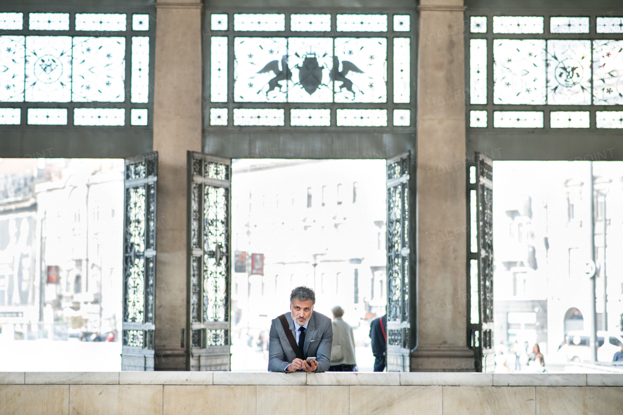 Handsome mature businessman with smartphone in a city. Man at the railway station.