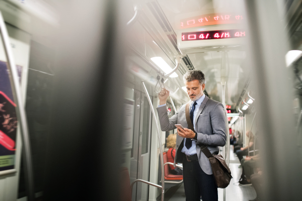 Handsome mature businessman in a city. Man with smartphone travelling by subway train.