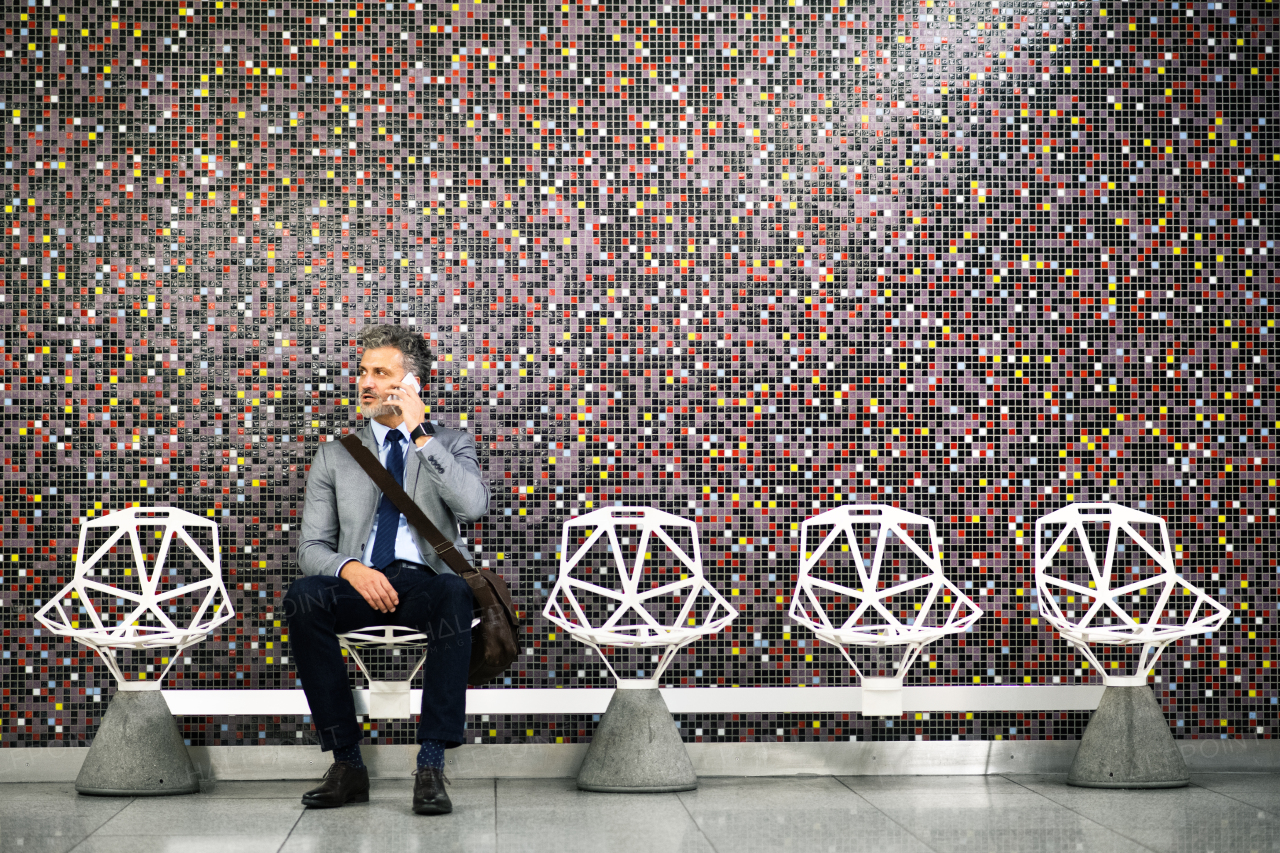 Handsome mature businessman in a city. Man with smartphone waiting for the train at metro station, making a phone call.