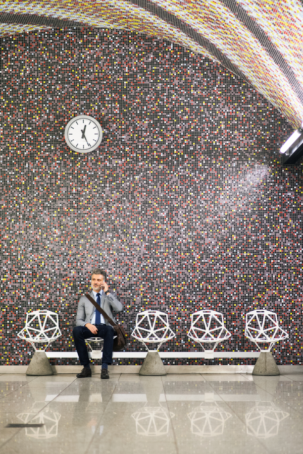 Handsome mature businessman in a city. Man with smartphone waiting for the train at metro station, making a phone call.