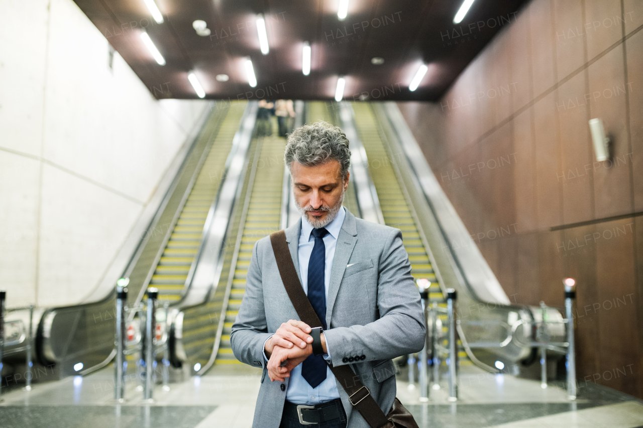 Handsome mature businessman in a city. Man standing in front of an escalators at the subway station, checking the time.