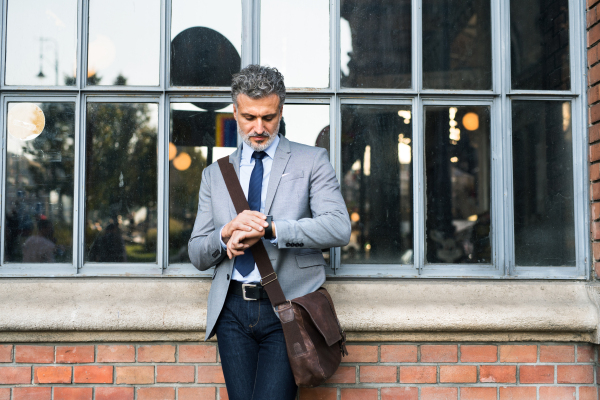 Handsome mature businessman standing in a city, checking the time.