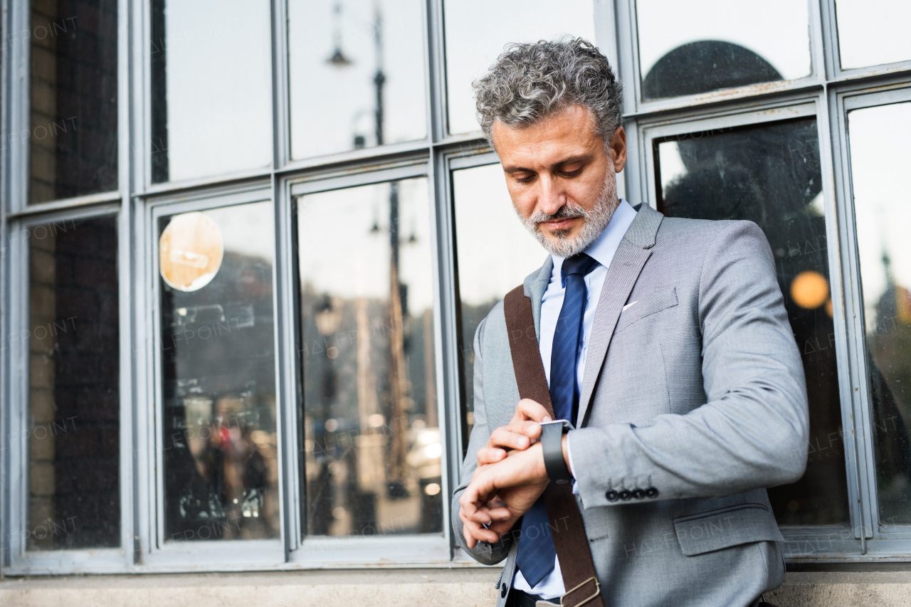 Handsome mature businessman standing in a city, checking the time.