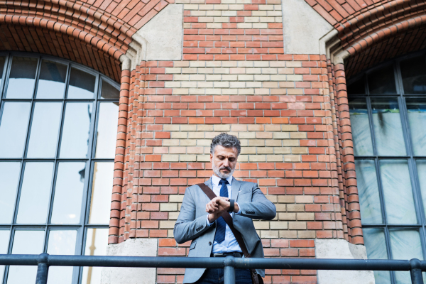 Handsome mature businessman standing in a city, checking the time.