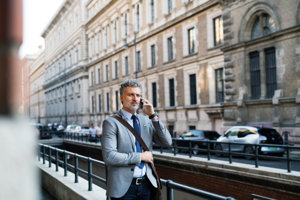 Handsome mature businessman with smartphone in a city, making a phone call.