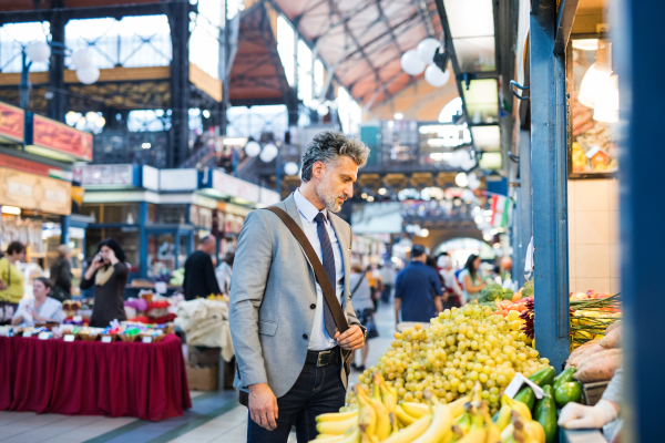 Handsome mature businessman in a city, buying fruit from a vendor. Blurred background.