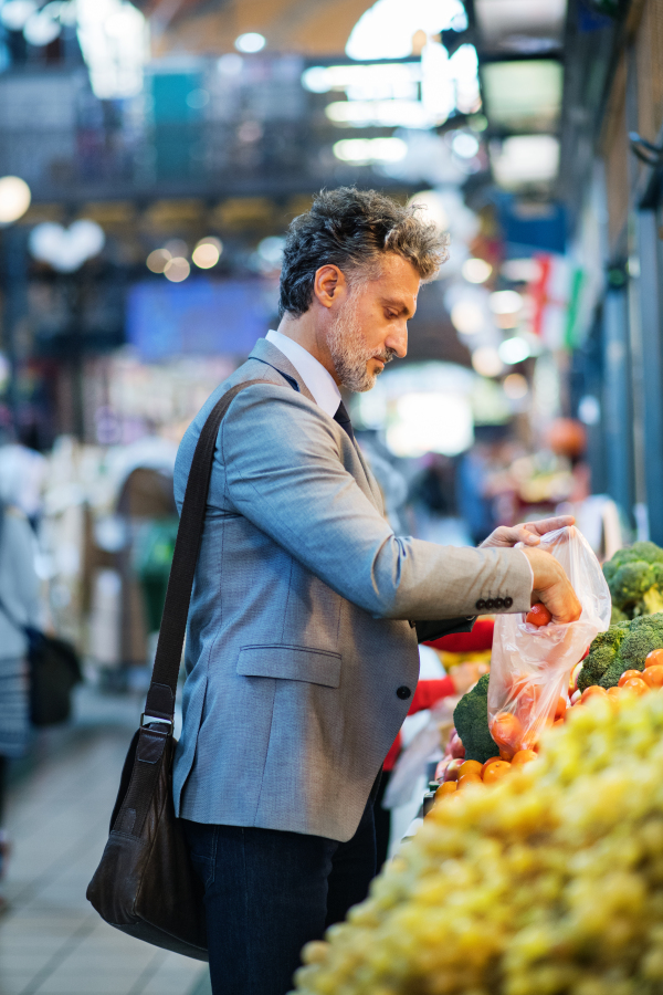 Handsome mature businessman in a city, buying fruit from a vendor. Blurred background.