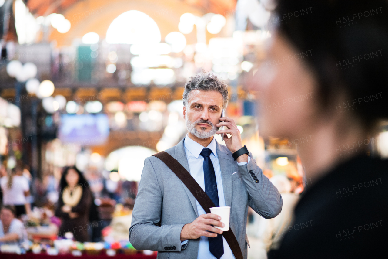 Handsome mature businessman with smartphone in a city, making a phone call. Blurred background.