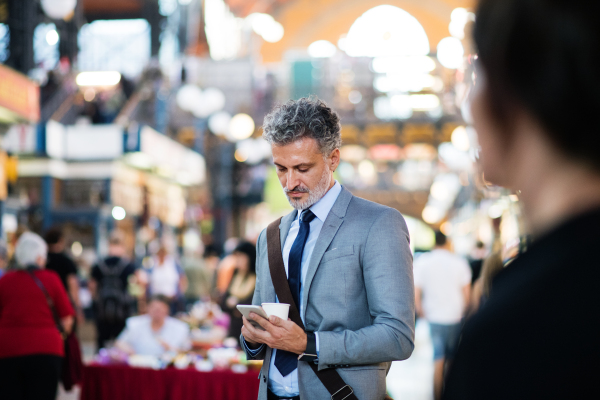 Handsome mature businessman with smartphone in a city, text messaging. Blurred background.