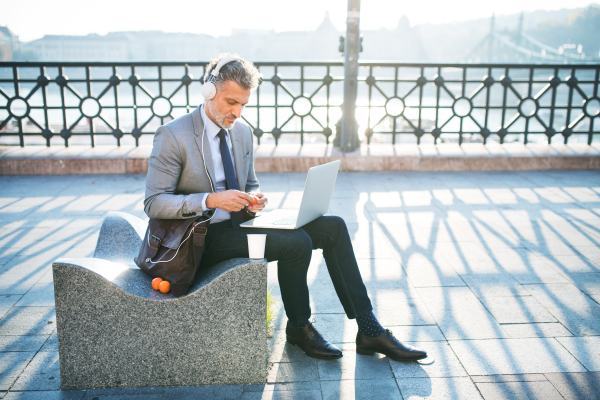 Handsome mature businessman with laptop and headphones in a city.