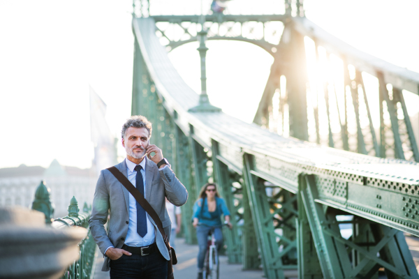 Handsome mature businessman with a smartphone in a city. Man walking on a bridge, making a phone call.