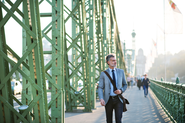 Handsome mature businessman in a city, walking on the bridge.