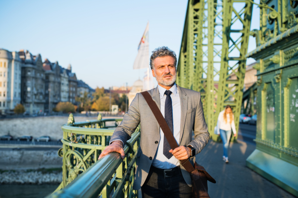 Handsome mature businessman in a city, walking on the bridge.