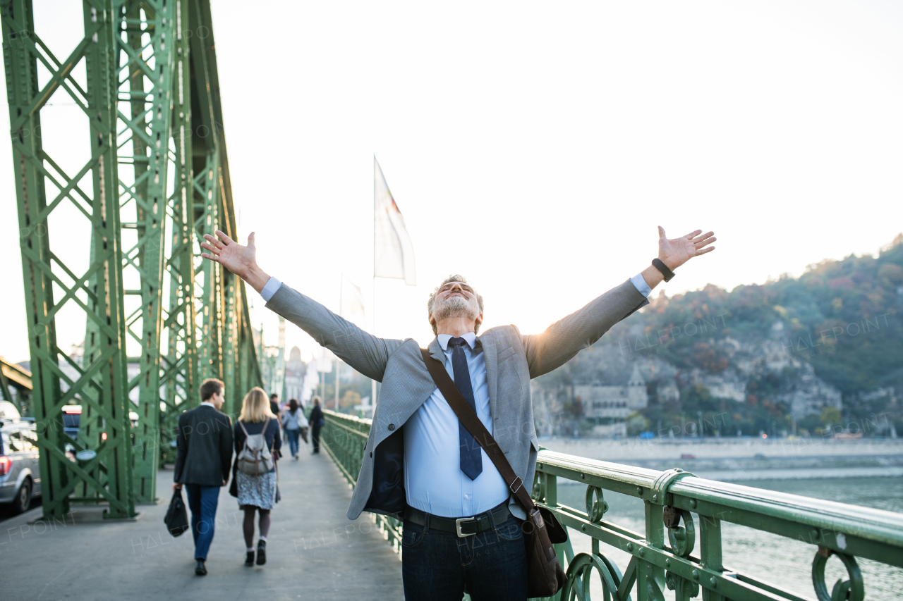 Handsome mature businessman in a city standing on the bridge, stretching arms.